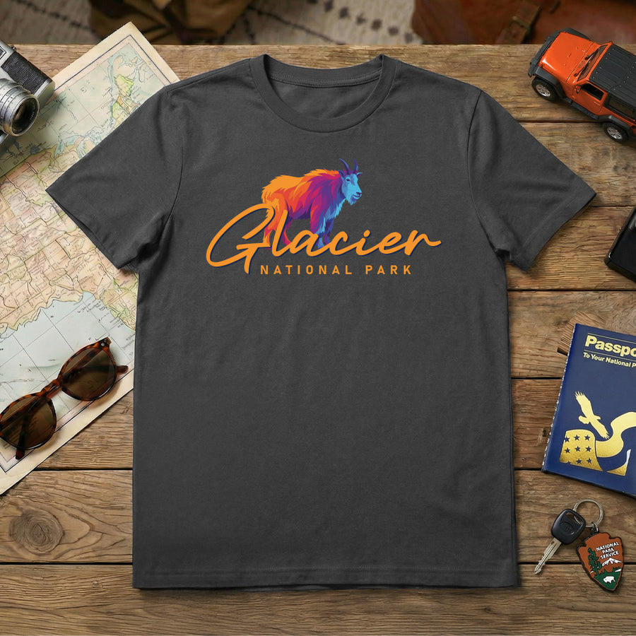 The Glacier – Mountain Goat Script T-Shirt in charcoal gray features a vibrant mountain goat graphic, making it an ideal Montana souvenir for adventurers and fans of Glacier National Park.