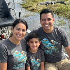 Family of three wearing Florida National Parks Pelican Charcoal T-shirts on a boat in the Everglades