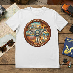 White t-shirt with steering wheel Route 66 inspired design on a wooden table with travel items.